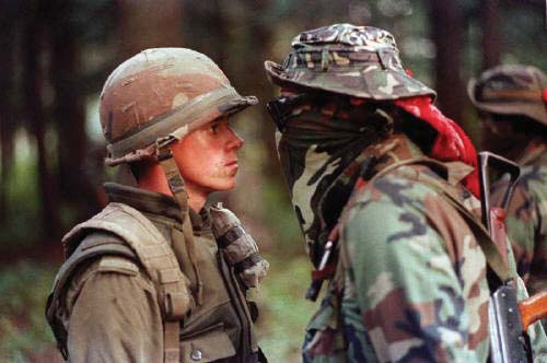 A soldier stares down a person dresseed in a face mask and sunglasses