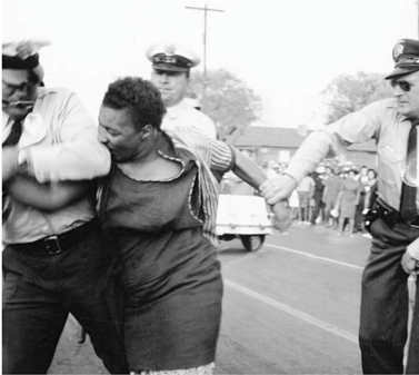 A black woman bites the arm of a white officer arresting her.