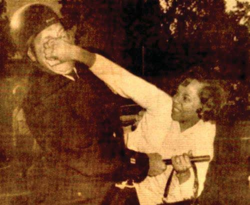 An old sepia tone photo seemingly from the 1950s. A black woman punches a white police officer in the face.