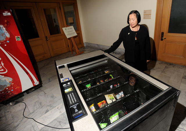 A woman looks at a tipped over vending machine inside a government building.